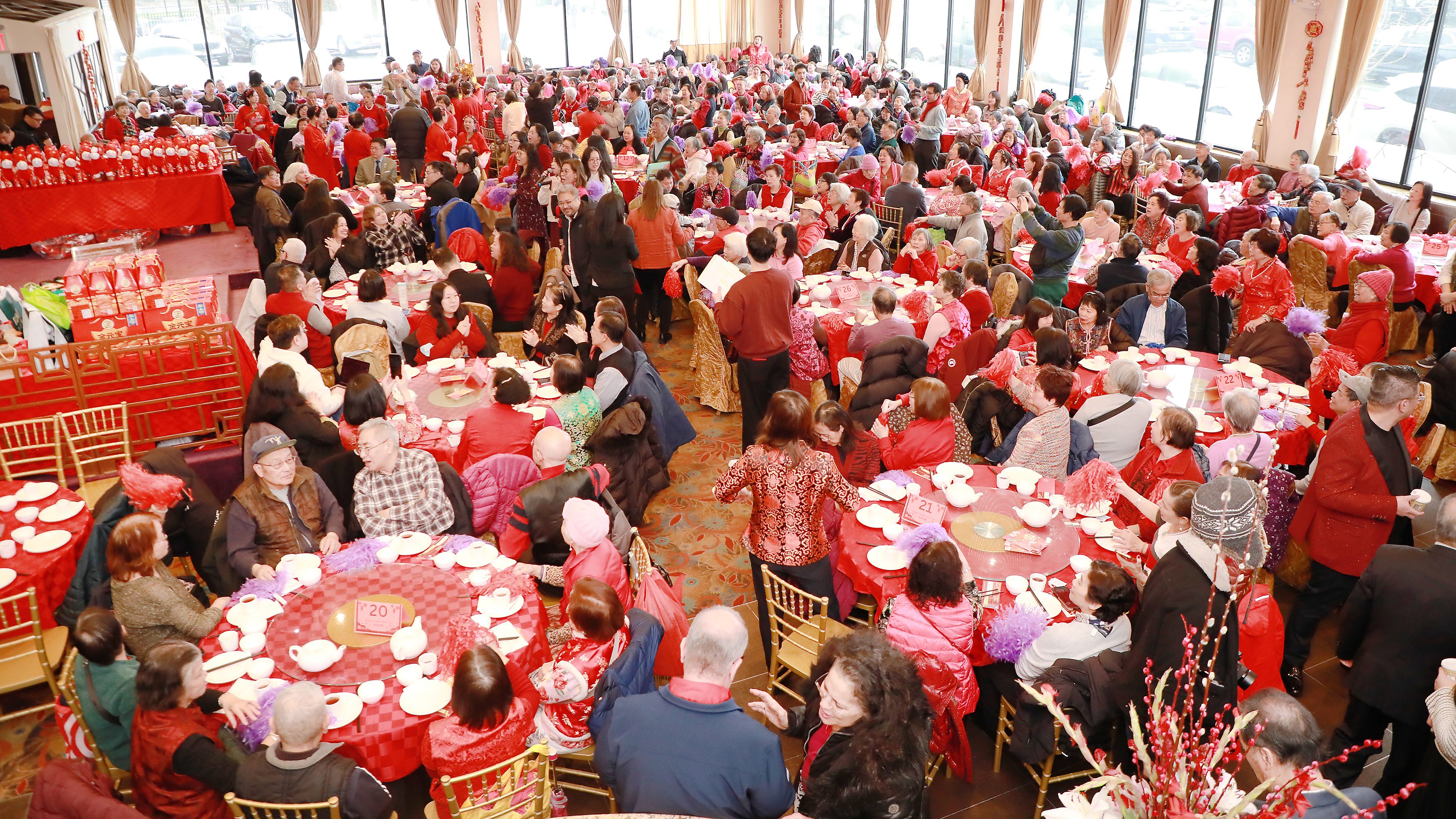 一个装饰华丽的宴会厅，座无虚席，数百人身穿红色服装，围坐在圆桌旁，正在庆祝节日。窗外可见车流，场景生动热闹。