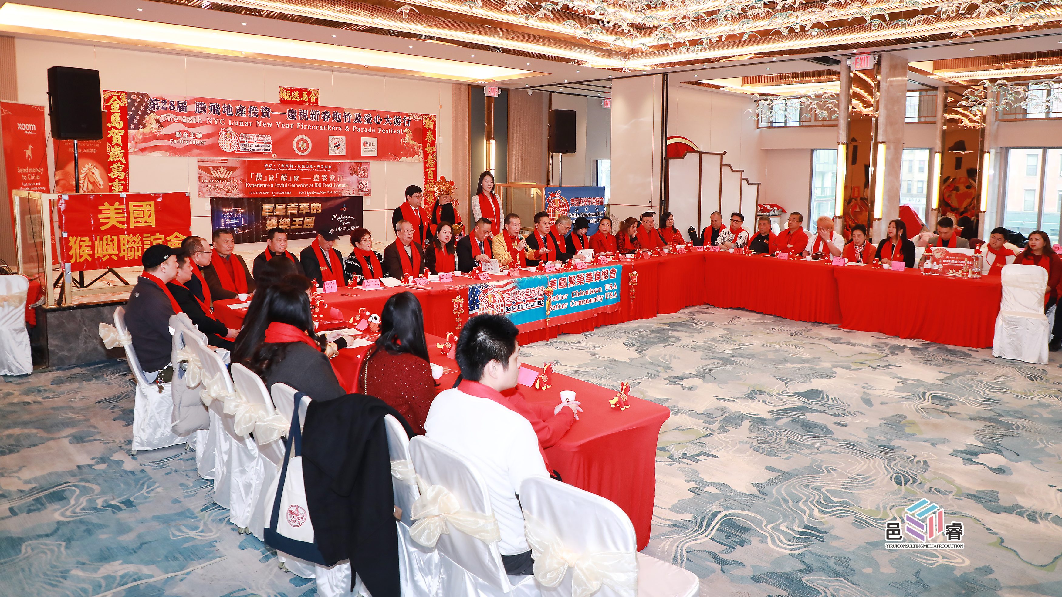 中国纽约春节烟花游行筹备会议,参会人员穿着红色服装,圆桌上摆满了装饰品和广告展板。