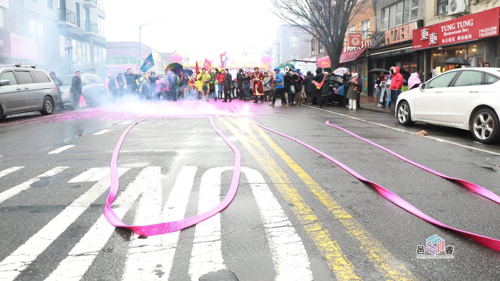 街道上,烟雾缭绕,彩带散落,庆祝活动正在进行,观众们在街道两旁观看。